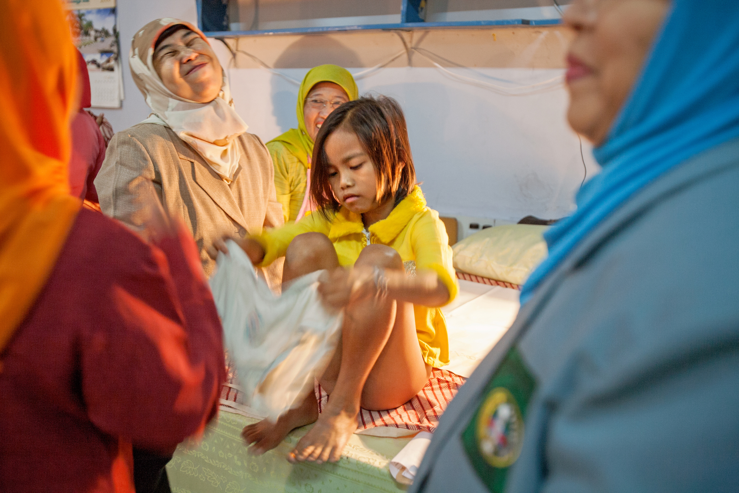 Surrounded by her circumcisers, a young girl is helped back into her underwear after the procedure in Bandung, Indonesia.